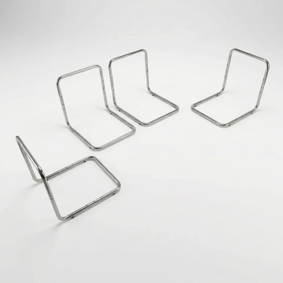 Four chrome tube L-shaped seat frames at different angles on a pale gray studio floor, one tipped onto its back
