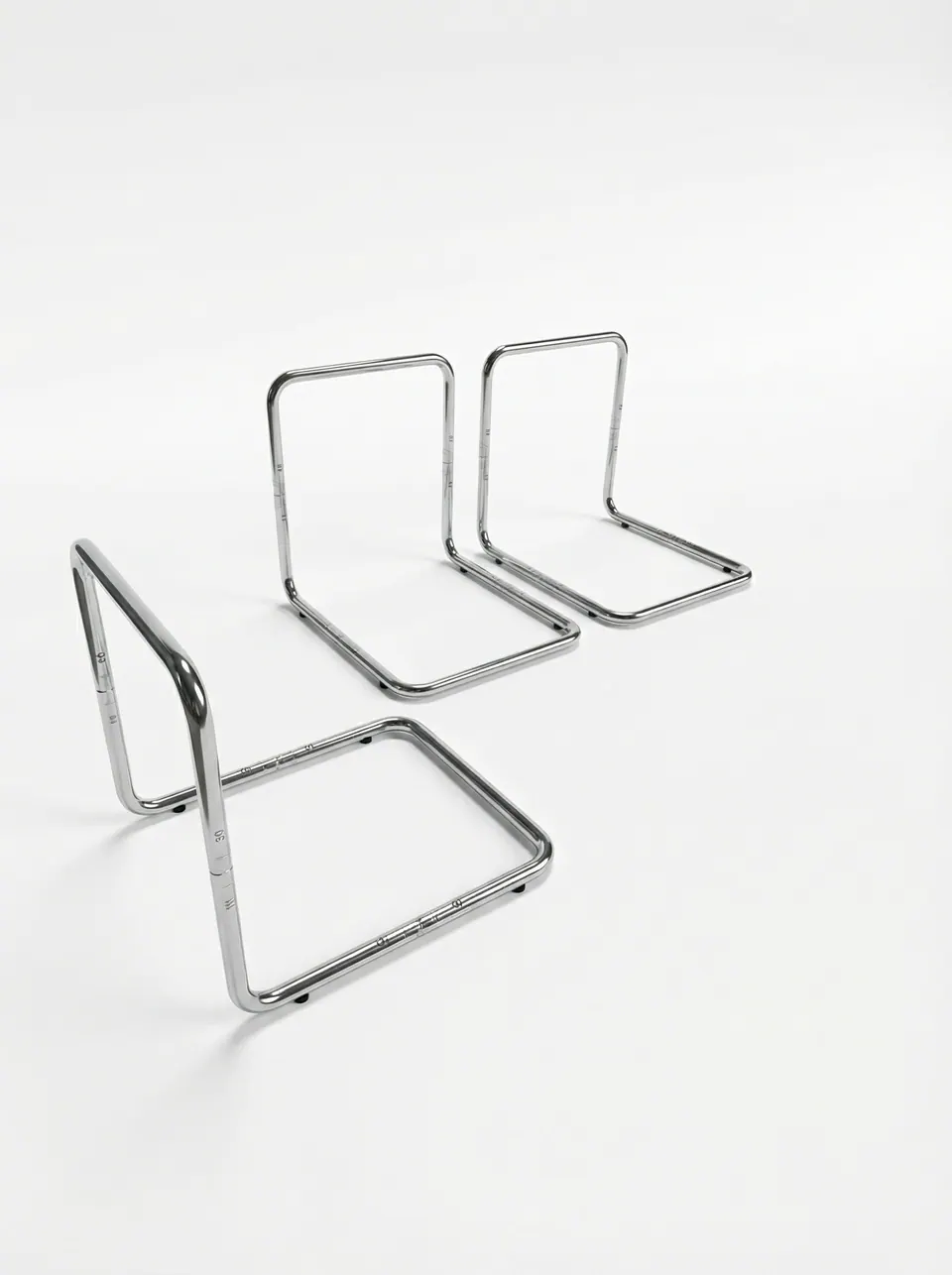 Three chrome tubular L-frames in a row on light gray, the nearest tipped forward to show its square base and rubber feet
