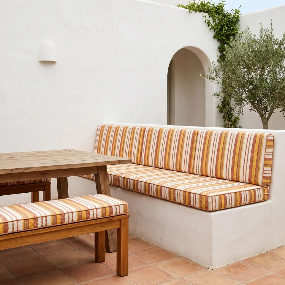 Terracotta, saffron and cream striped seat and back cushions on a white masonry banquette in a tiled courtyard