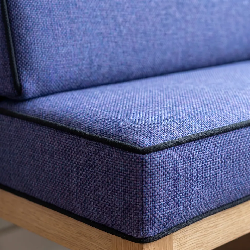Close-up of a violet-blue woven banquette seat and backrest cushion with thin black piping on a light oak frame