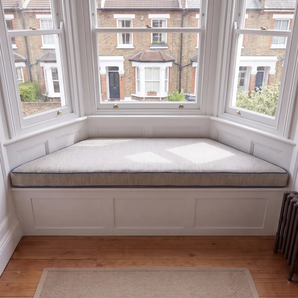 Oatmeal linen-look trapezoid cushion with thin indigo piping on a white paneled Victorian bay window seat