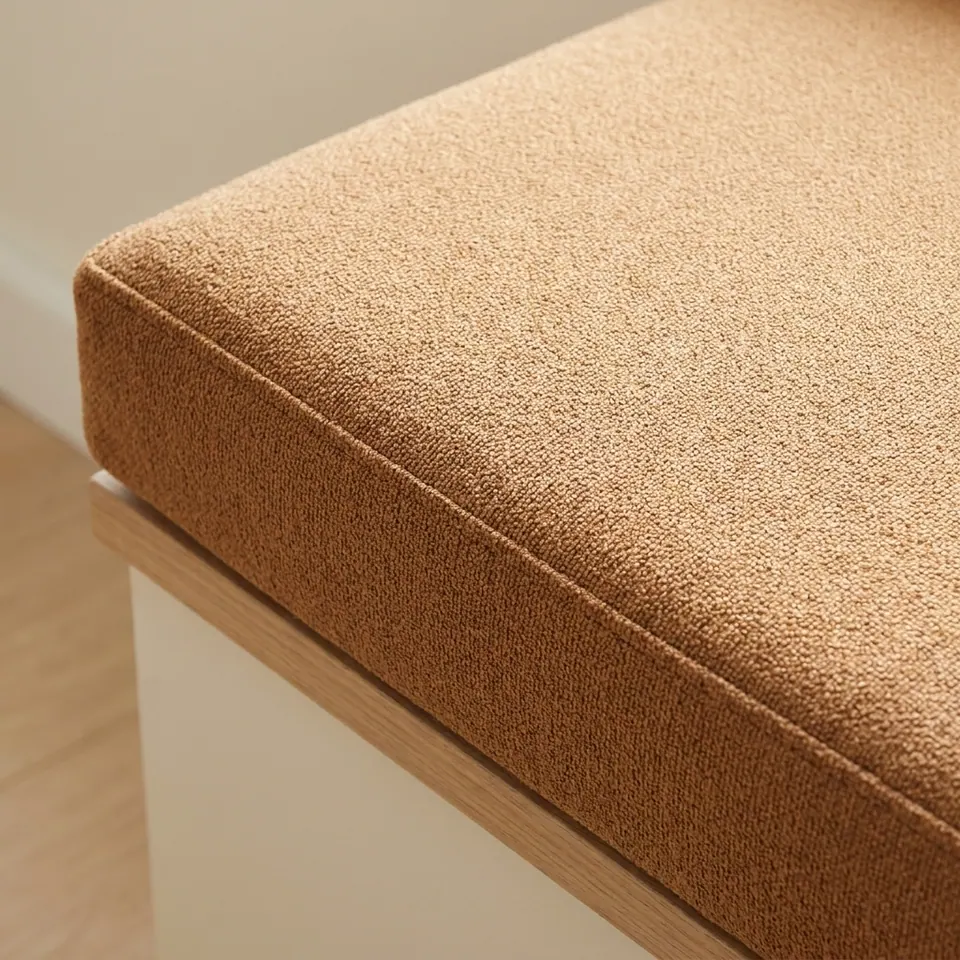 Close-up of an unpiped caramel bouclé box cushion corner on a white bench with an oak top edge