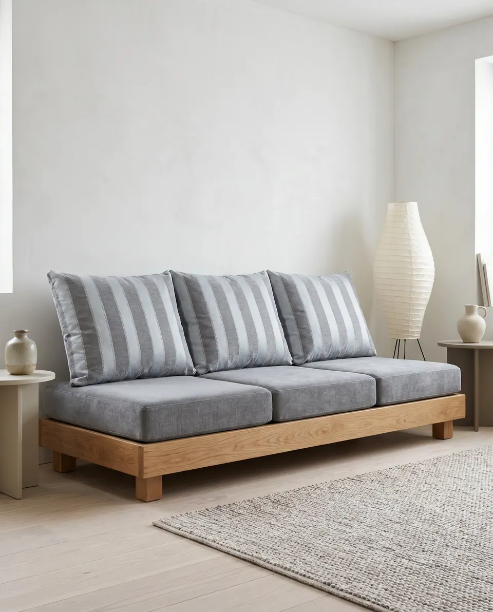Charcoal seat cushions with three gray and white striped back pillows on a low oak platform sofa in a limewashed room