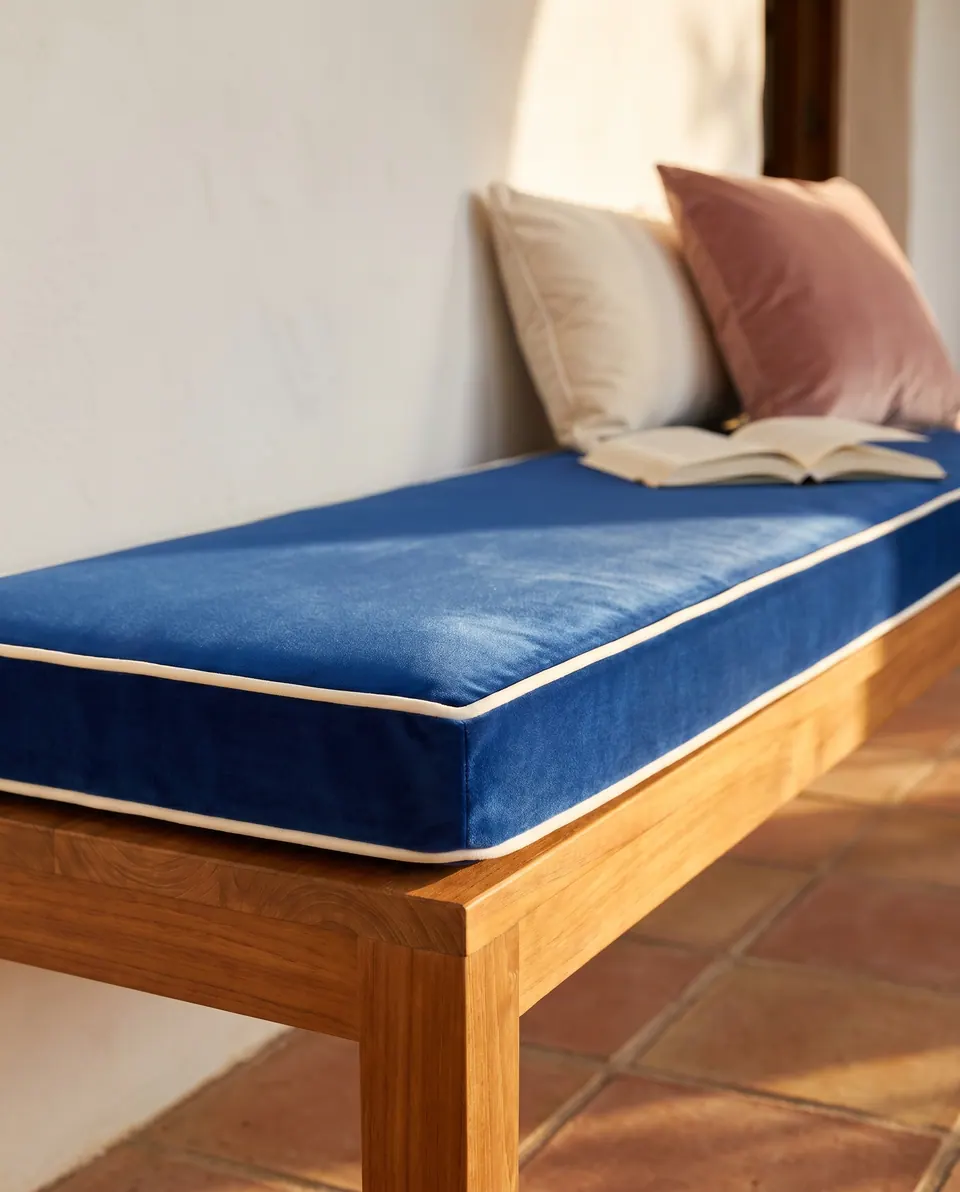 Cobalt blue velvet bench cushion with ivory piping on a teak bench with cream and pink pillows on terracotta tiles