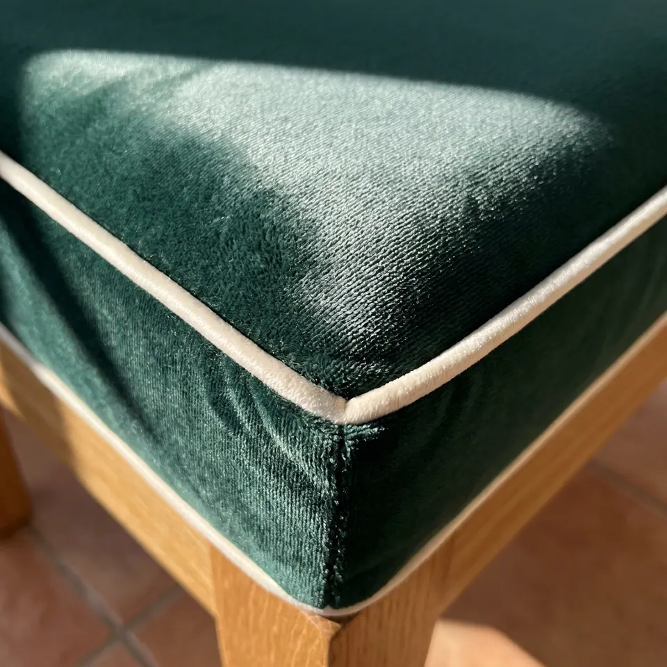 Close-up of an emerald velvet box cushion corner with ivory contrast piping on an oak frame over terracotta tiles
