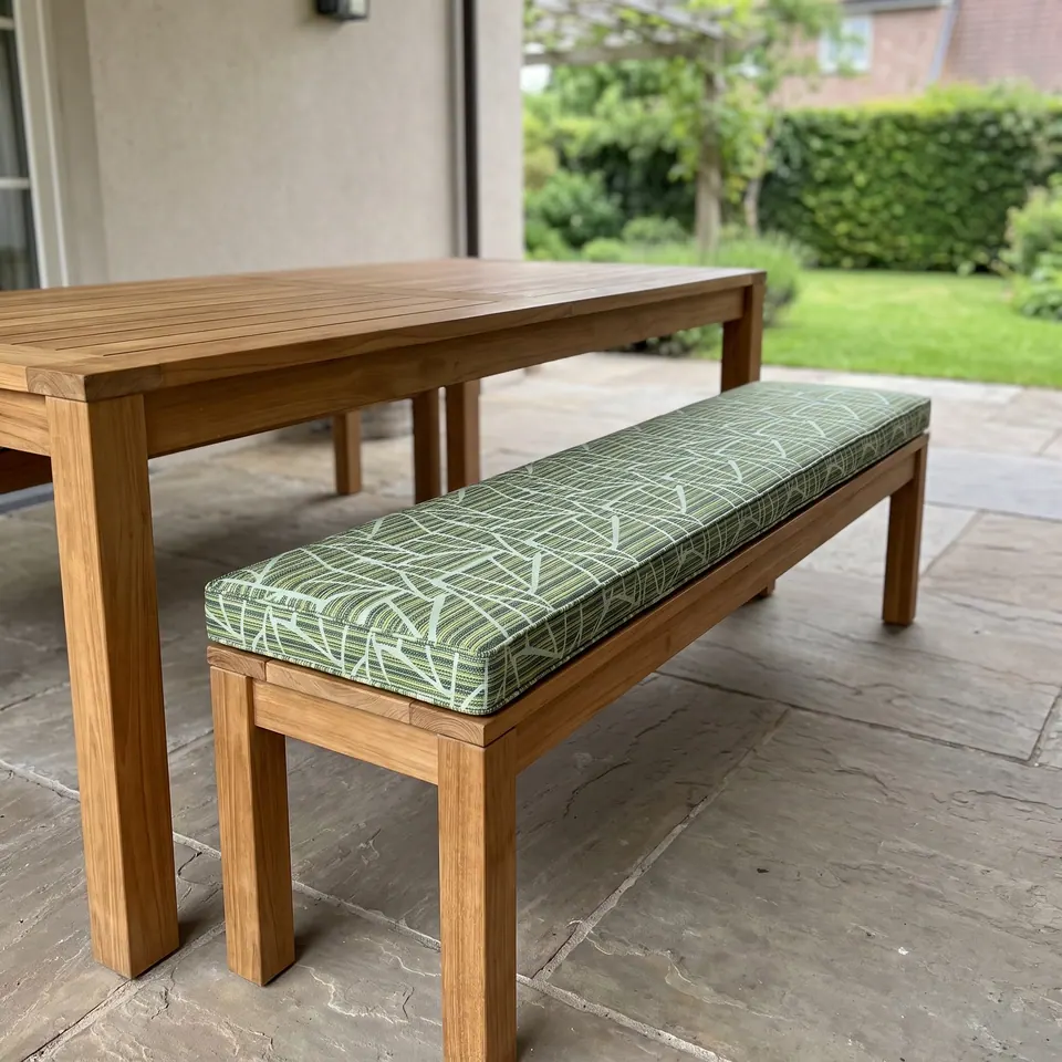 Green and white leaf-line print box cushion on a teak dining bench beside a teak table on a stone patio