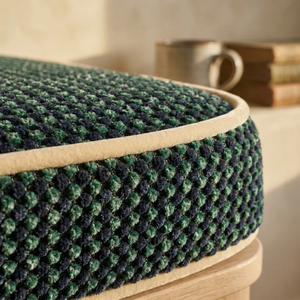 Rounded corner of a forest green and navy dotted chenille cushion edged in cream velvet piping on an oak base