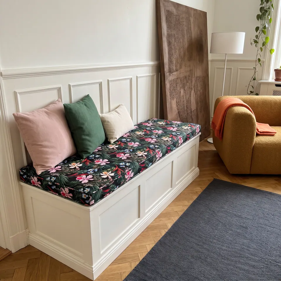 Dark green hibiscus print cushion on a white paneled storage bench with blush, emerald and cream pillows