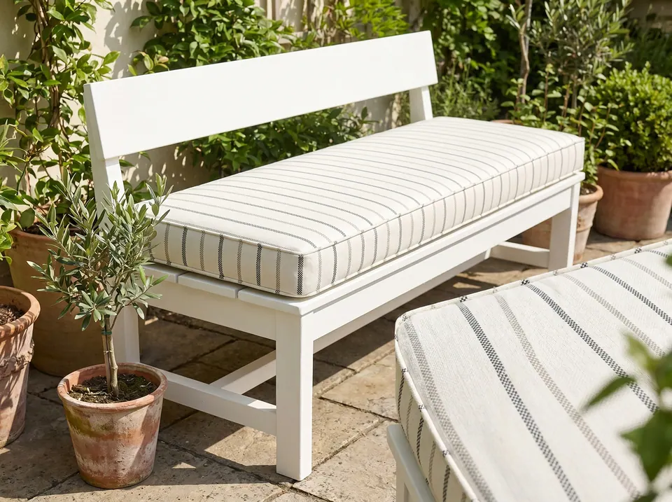 Ivory bench cushion with charcoal ticking stripes on a white-painted garden bench among terracotta pots and olive