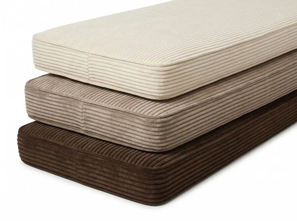 Light-to-dark stack of cream, taupe and chocolate corduroy bench cushions with piped edges on a white background