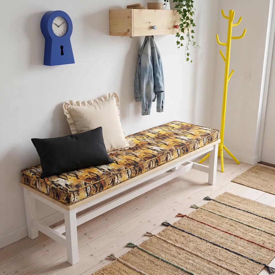 Ochre and black tiger collage print bench cushion on a white bench in an entry with a blue clock and yellow coat stand