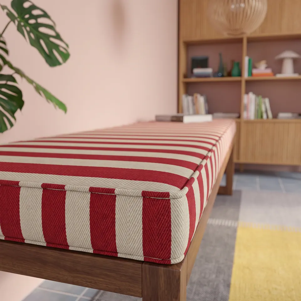 Low-angle close-up of a red and cream herringbone striped bench cushion showing its self-piped box corner