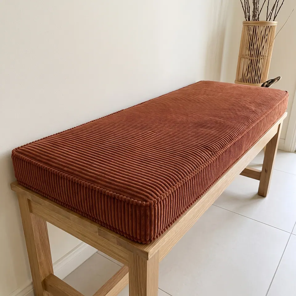 Rust terracotta corduroy box cushion with self piping on an oak bench in a bright tiled entryway with a bamboo vase