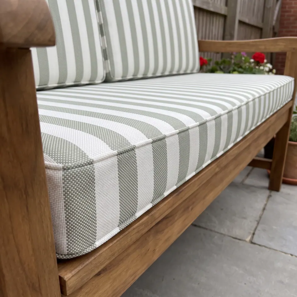 Close-up of a sage and white awning stripe box cushion with self piping on a teak garden bench seat