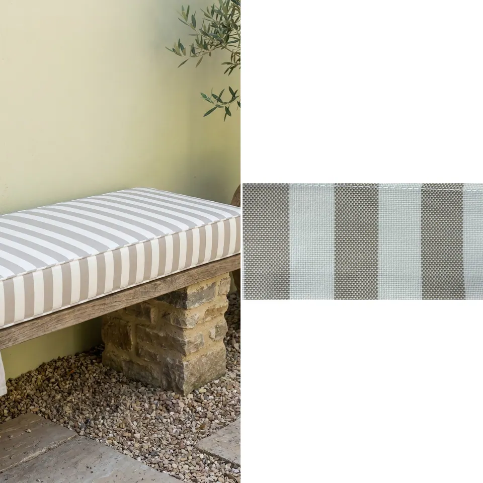 Taupe and white wide stripe box cushion on a rustic plank bench with stone piers against a pale sage wall, fabric strip