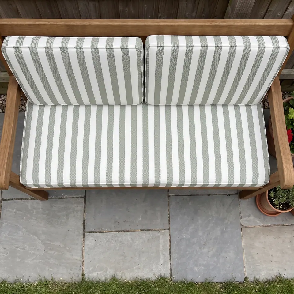 Overhead view of a teak garden bench with one sage and white striped seat cushion and two matching back cushions