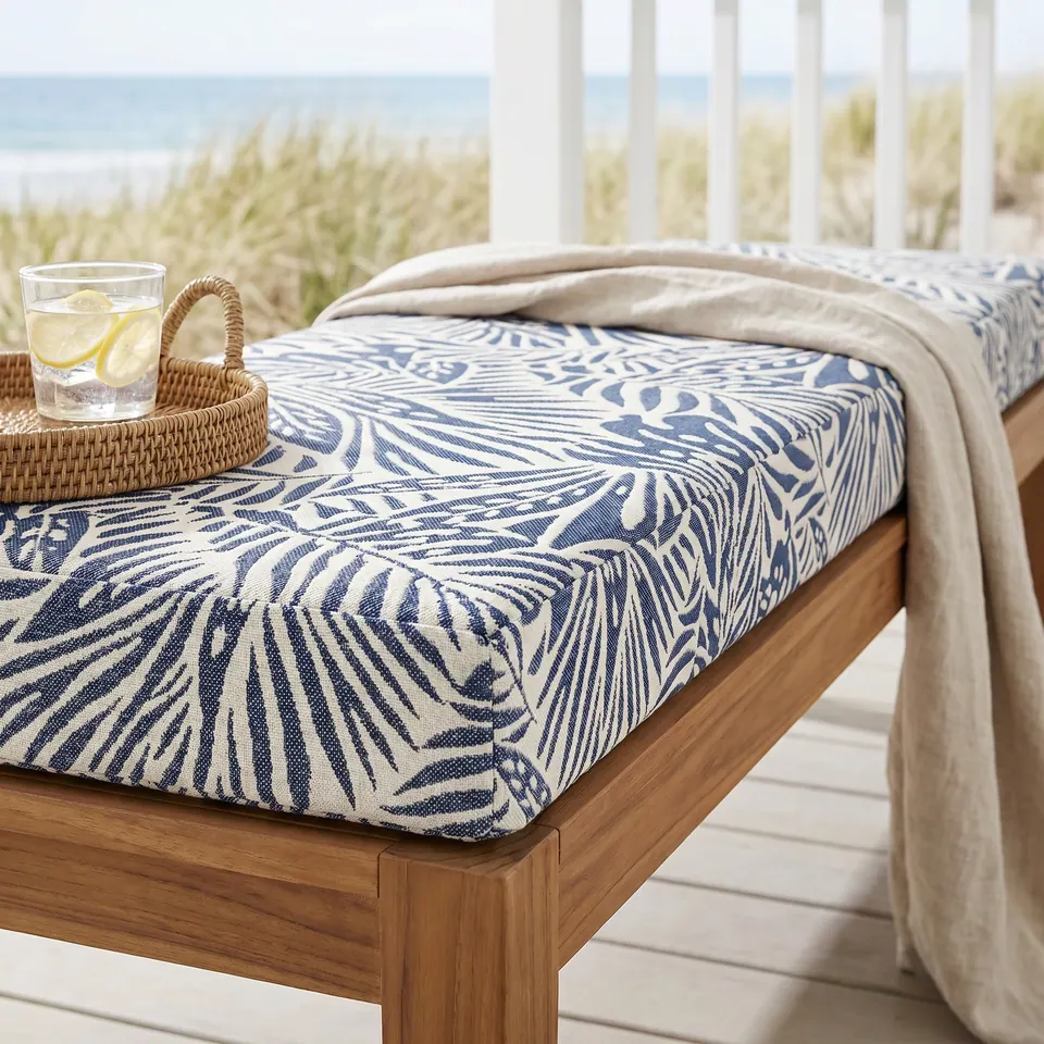 Navy and cream palm-leaf jacquard bench cushion without piping on a teak bench on a white beach-house porch, dunes behind