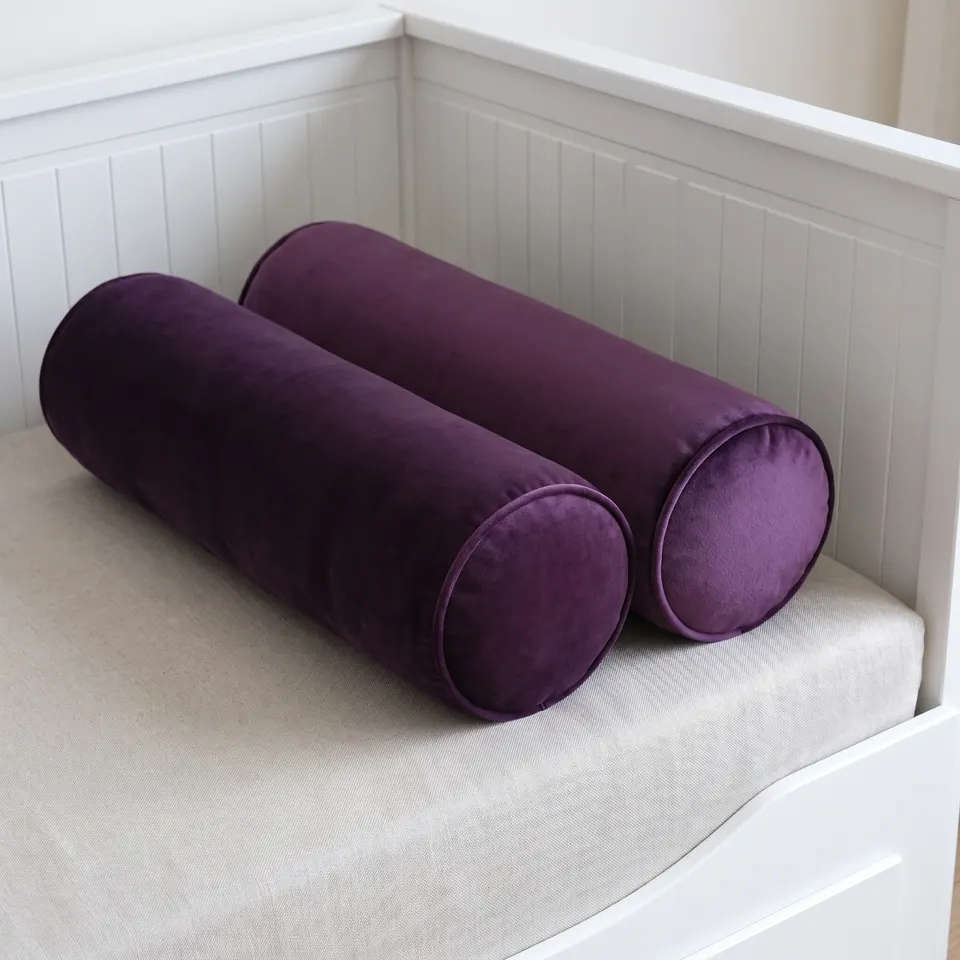 Two eggplant purple velvet bolsters with self piping side by side on a linen daybed cushion against white beadboard