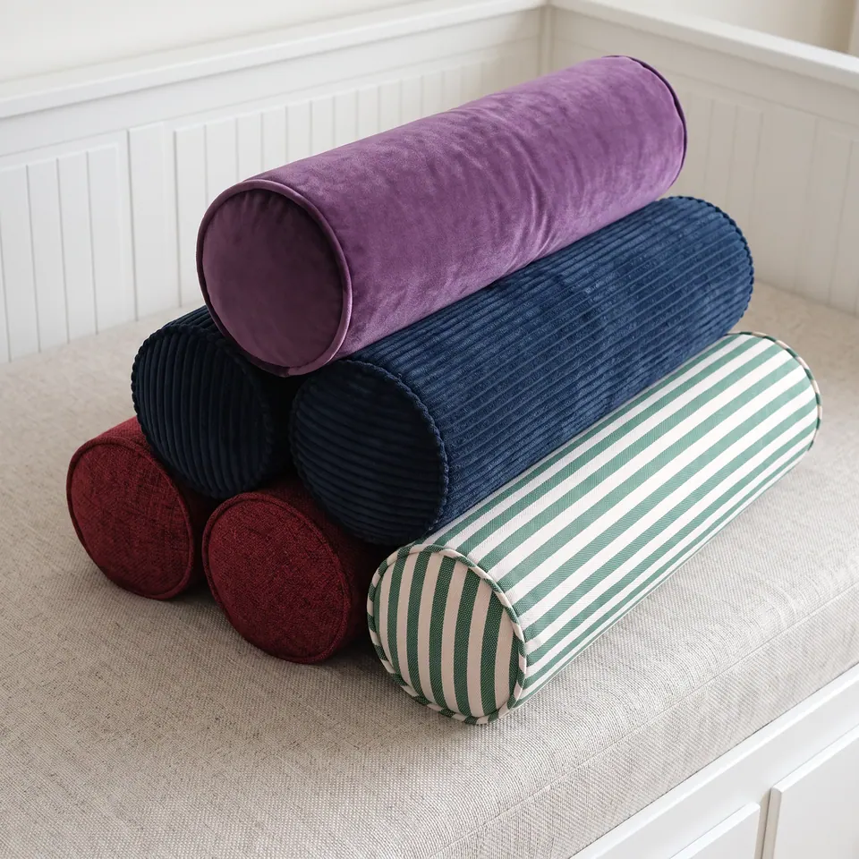 Stacked pyramid of bolsters on a linen daybed cushion: plum velvet on top, navy corduroy, burgundy tweed and green stripe
