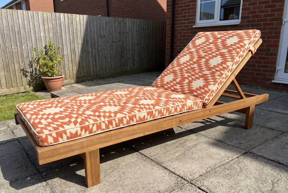 Terracotta and cream kilim-pattern sun lounger cushion with piping on a hardwood lounger on a paved back garden patio