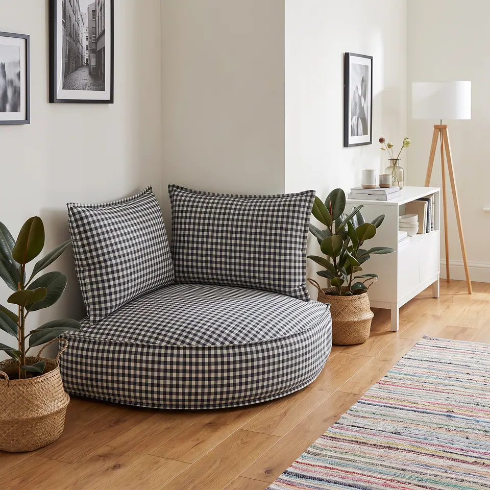 Black and white gingham corner floor cushion with two backrest pillows beside rubber plants in a bright oak-floored room