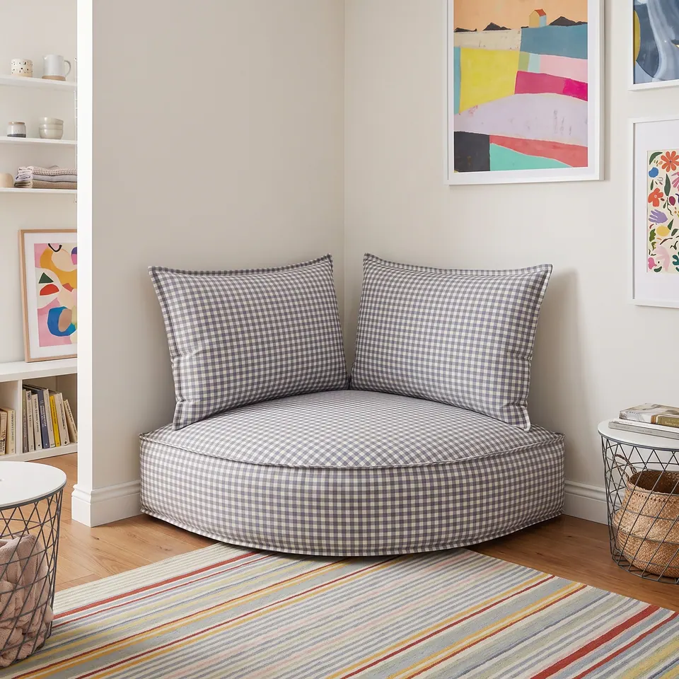 Gray and white gingham corner floor cushion with backrest pillows under bright abstract prints on a striped rug