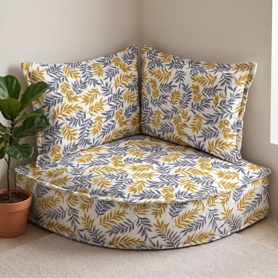 Gray and mustard gold leaf-print corner floor cushion with backrest pillows beside a fiddle-leaf fig in a white room