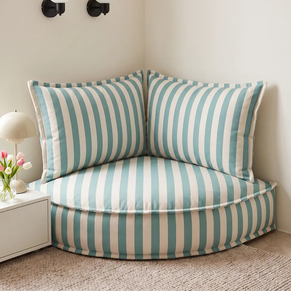 Light teal and cream striped corner floor cushion with two backrest pillows next to a white nightstand with tulips