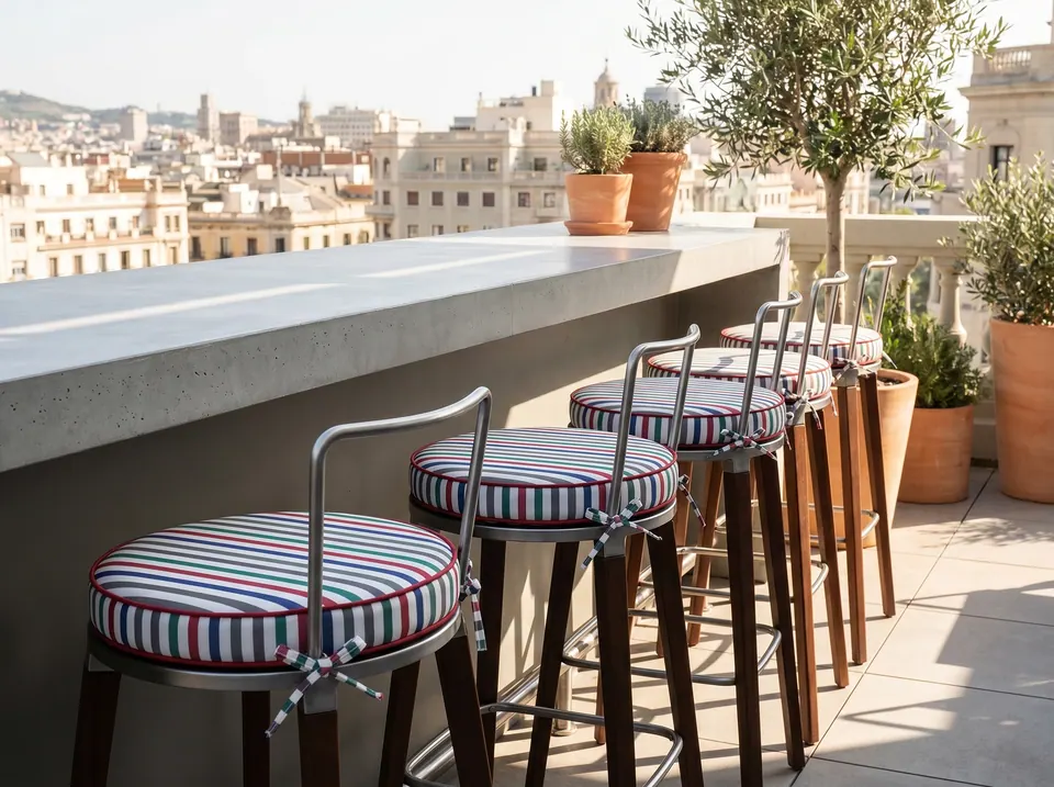 Round box cushions in red, green and navy stripes on a row of bar stools at a rooftop terrace counter above the city