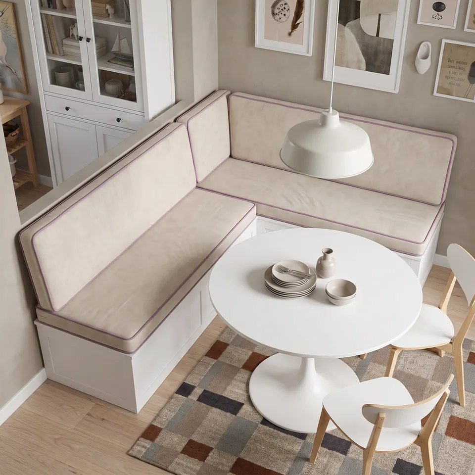 Overhead view of ivory velvet L-shaped banquette cushions with lilac piping around a white tulip table on a patchwork rug