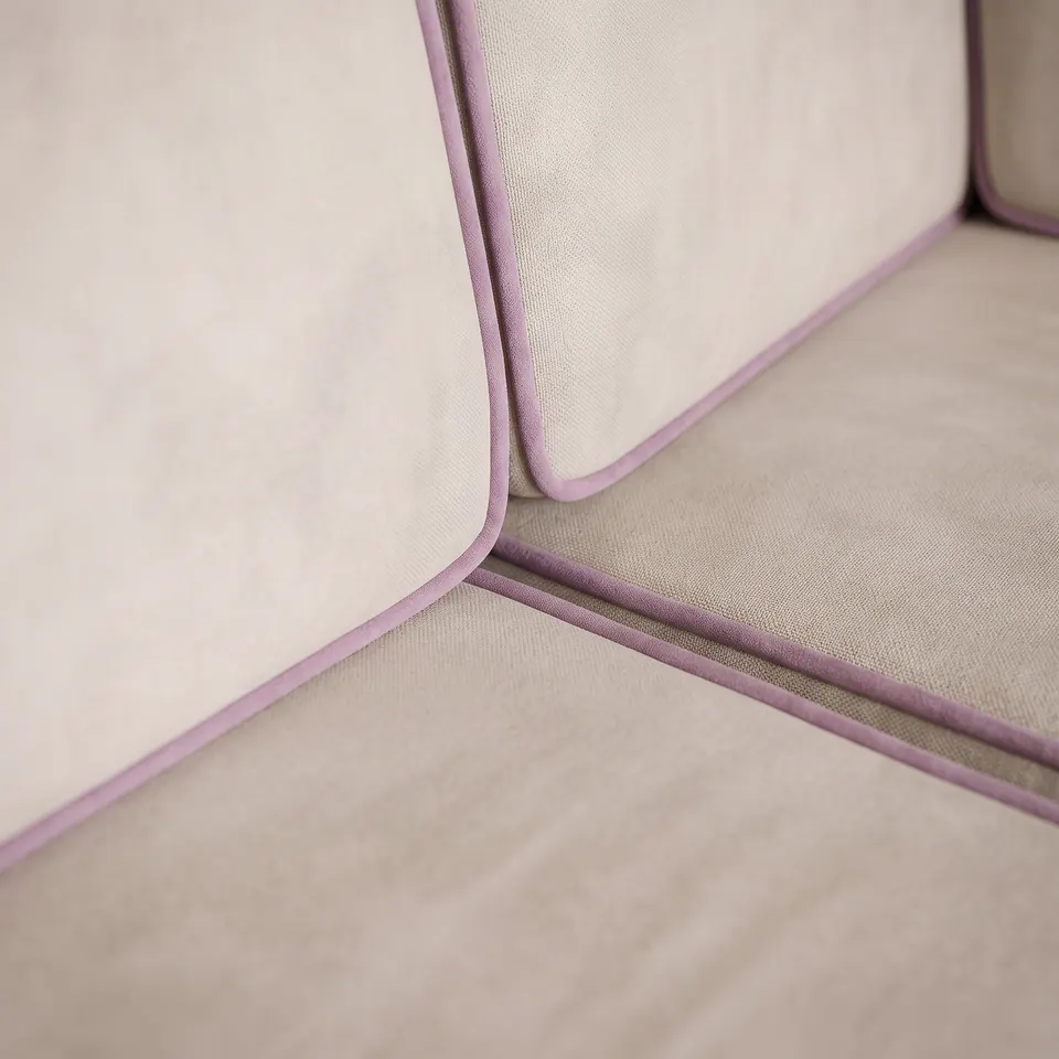 Macro detail of lilac velvet piping sewn into ivory velvet back and seat cushions at the corner of a banquette