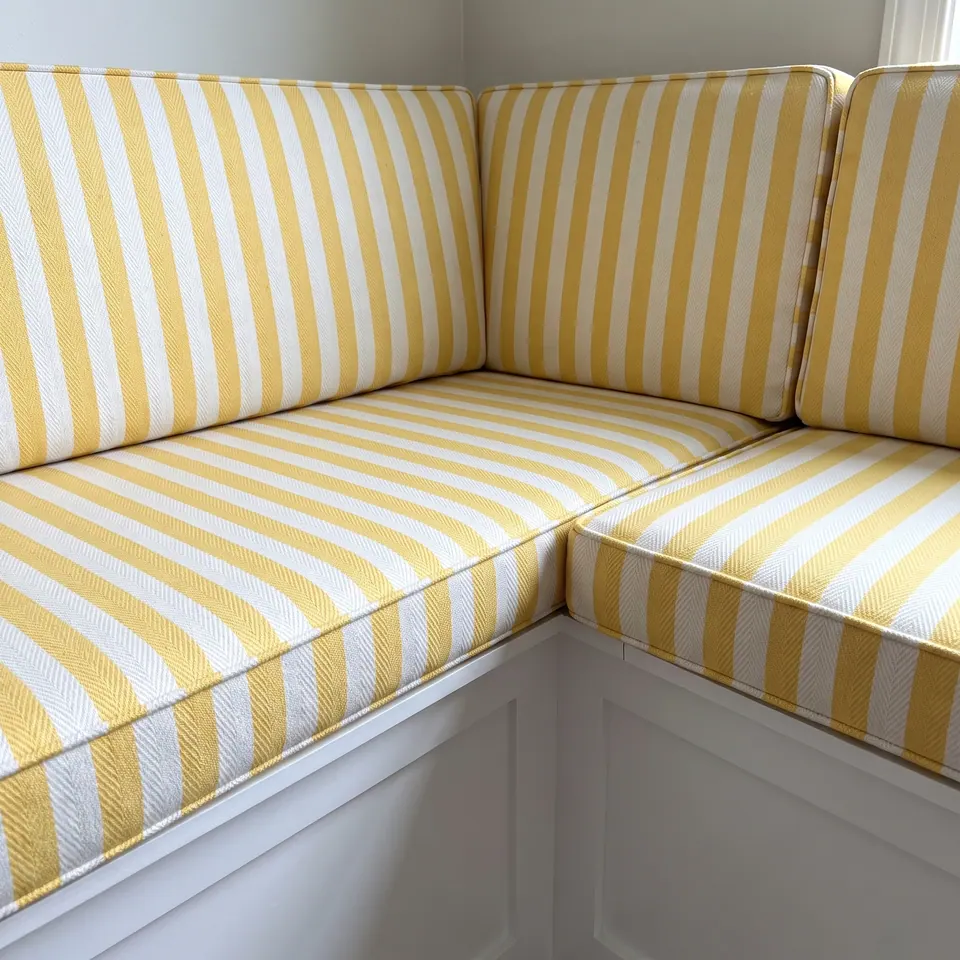 Close view of yellow and white herringbone-weave striped corner banquette cushions with self-piping on a white bench