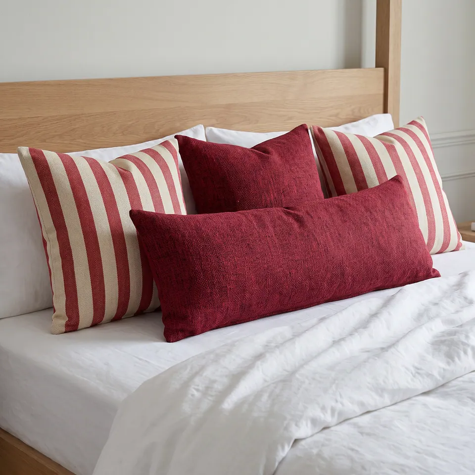 Crimson slubbed lumbar pillow before crimson-and-cream wide-stripe squares on white linen, light oak bed frame