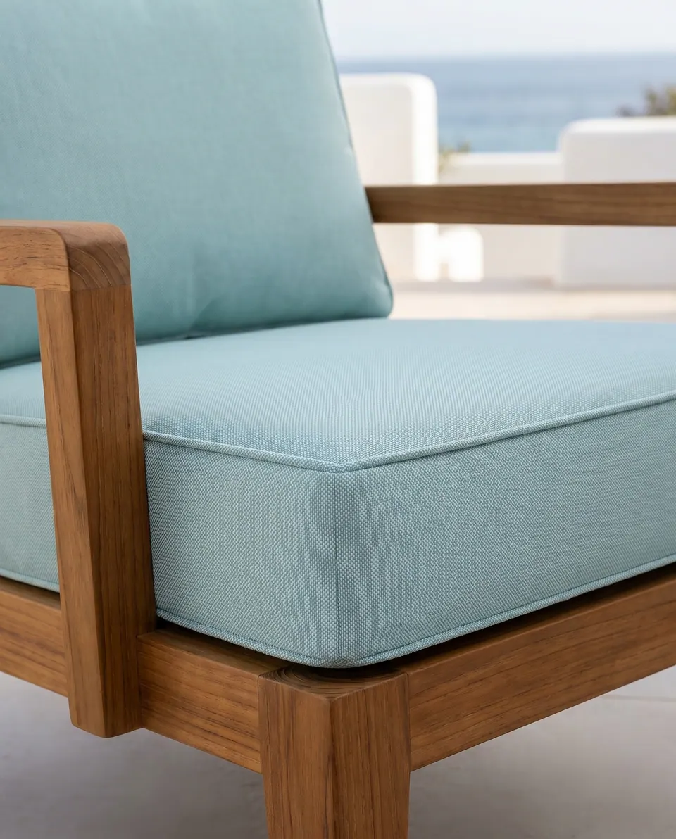 Aqua blue outdoor seat and back cushion on a teak lounge chair on a whitewashed terrace with a sea view