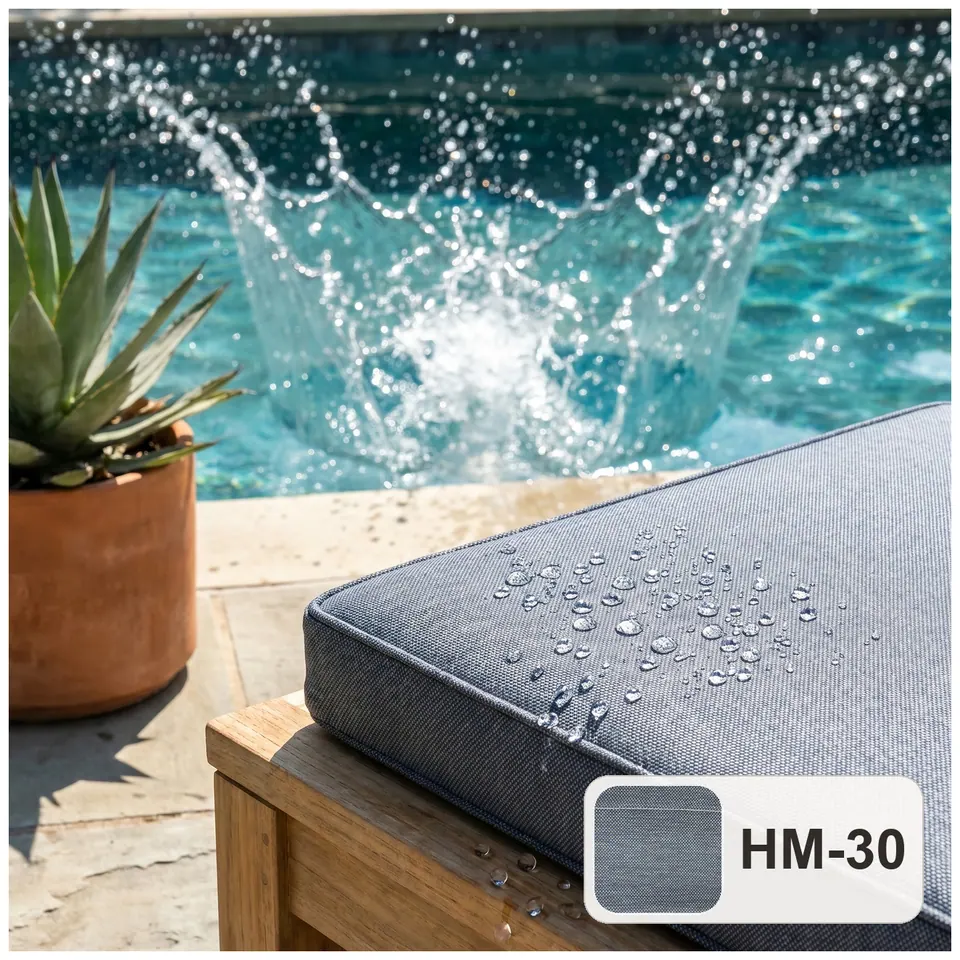 Water droplets beading on a slate gray water-repellent outdoor cushion on a teak frame beside a splashing pool