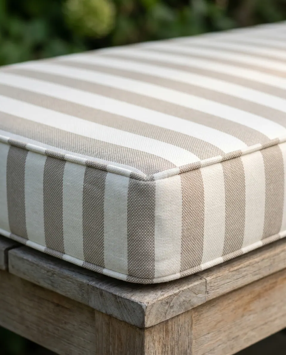 Close-up of a taupe and white striped outdoor cushion corner with piping on a silvered teak bench