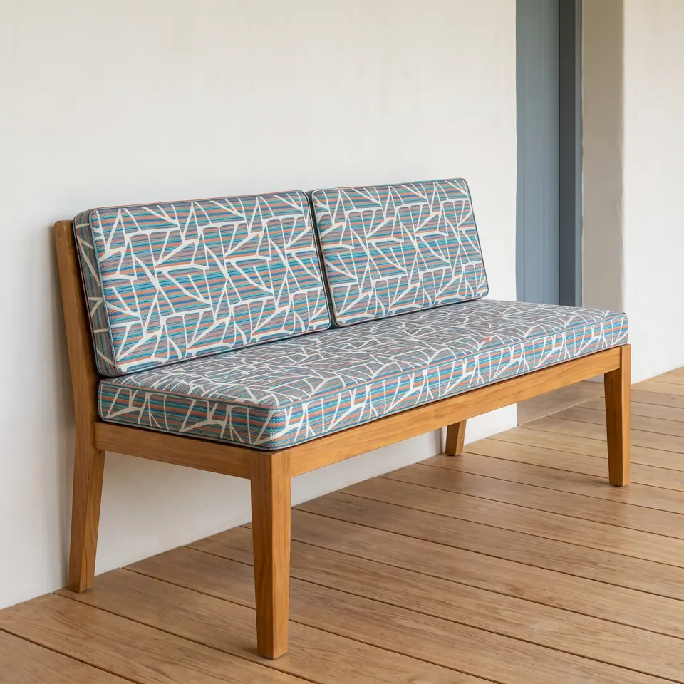 Teal, coral and gray geometric mosaic print seat and back cushions on a low-back teak bench on a wooden deck