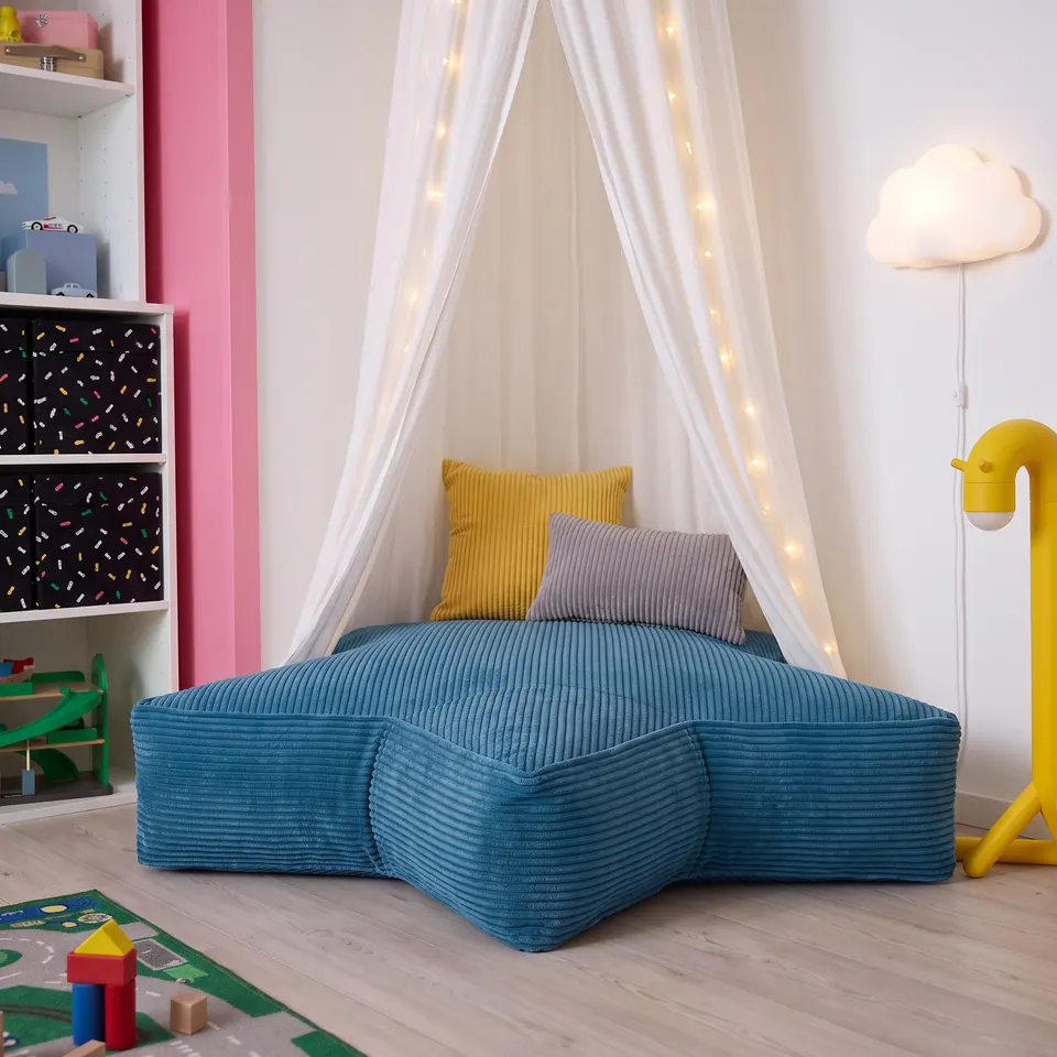 Front view of a petrol blue corduroy star floor cushion with an upright mustard pillow and gray lumbar under a canopy