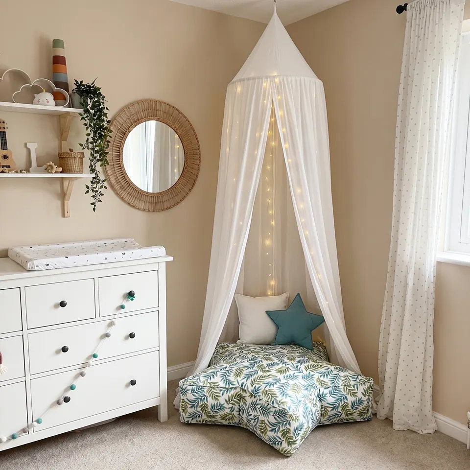 Fern print cotton star pouf under a fairy-light canopy in a beige nursery beside a white changing dresser and rattan mirror