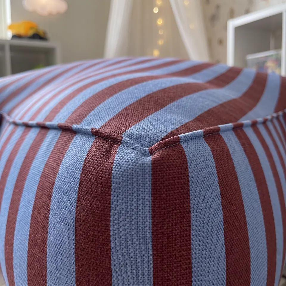 Close-up of a periwinkle blue and maroon awning-stripe star pouf corner with matching striped piping