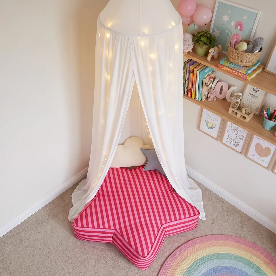 Overhead view of a pink and raspberry striped star floor pouf filling a carpeted kids' room corner beside a rainbow rug