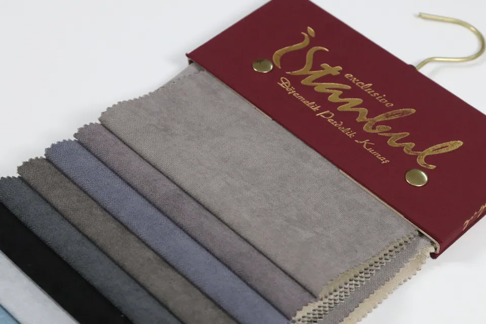 Fanned upholstery swatch book open on a warm dove gray sample, with charcoal, black and ice blue strips below