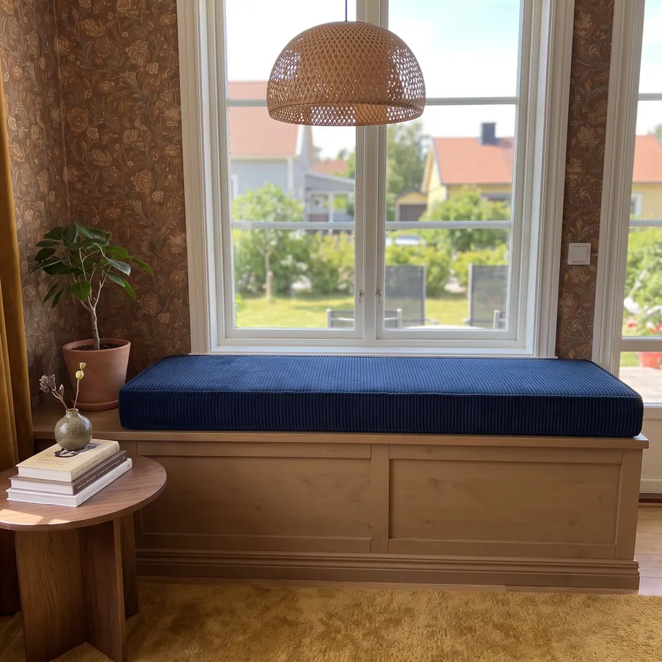 Pinned: Front view of a navy corduroy box cushion on a pine paneled window seat below a rattan dome pendant and garden window