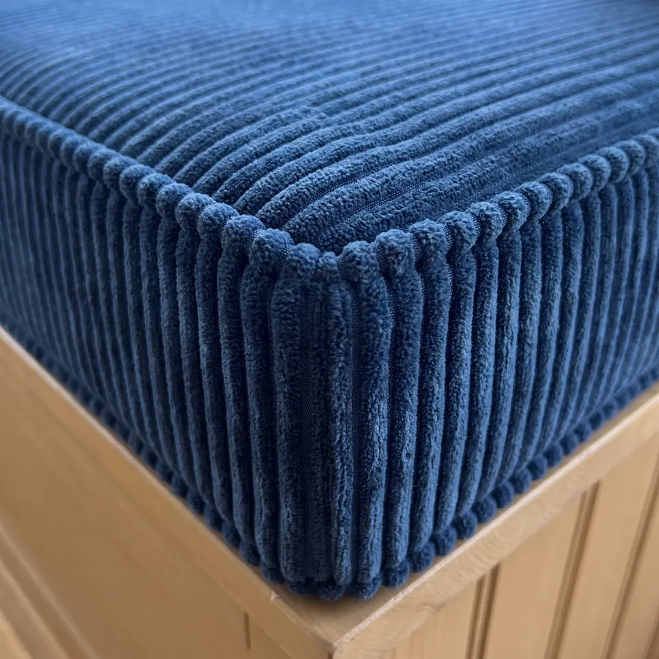 Macro close-up of navy wide-wale corduroy with beaded self piping and a sharp box corner on a pine seat