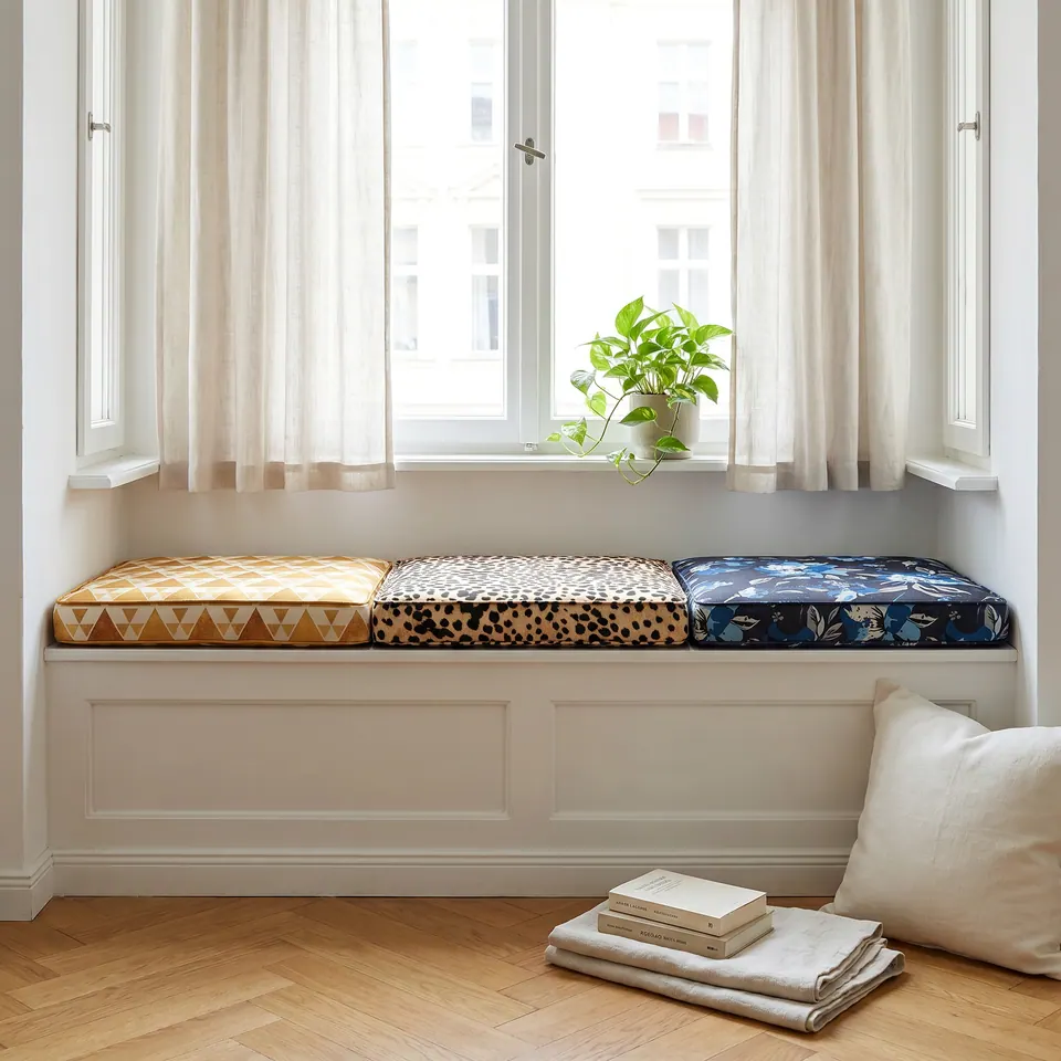 Three box cushions side by side on a white window bench: mustard triangle, cheetah spot and navy floral prints